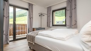 A bedroom with a bed, a window, a coat rack, and a view of a balcony. - Hofers Herzstück (Hinterglemm)