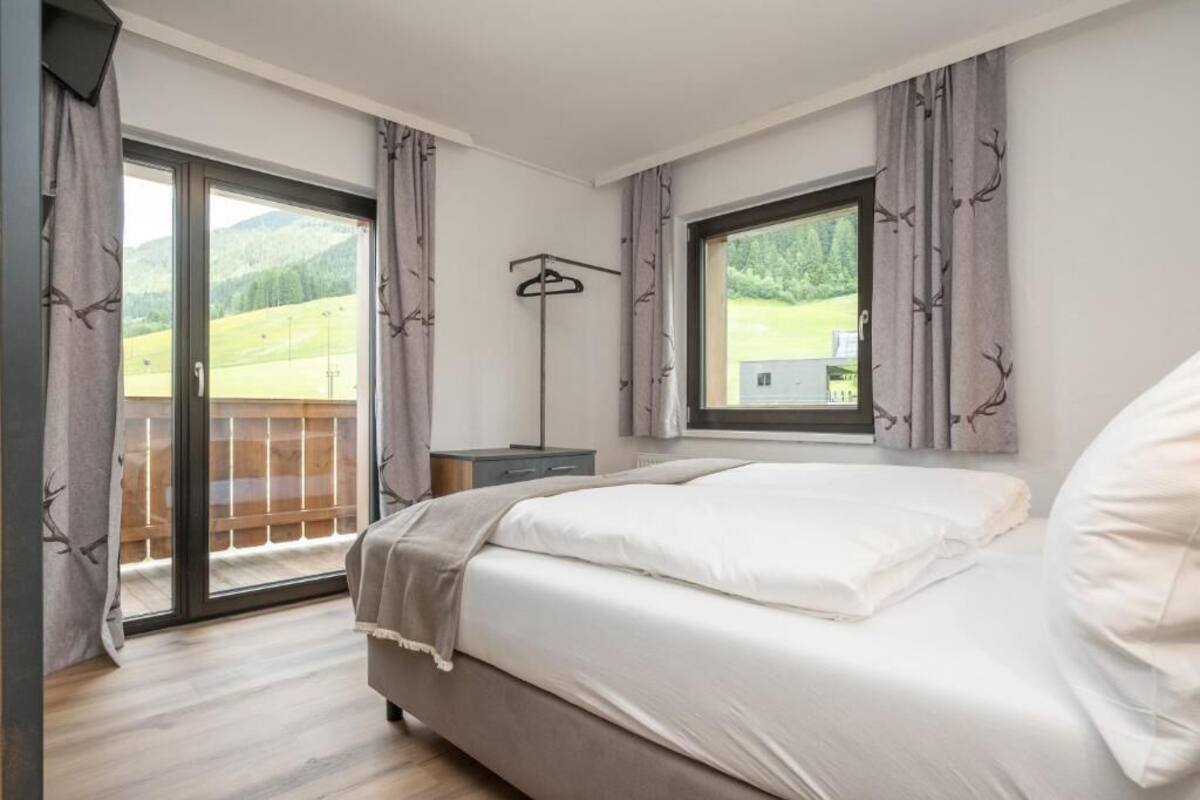 A bedroom with a bed, a window, a coat rack, and a view of a balcony.