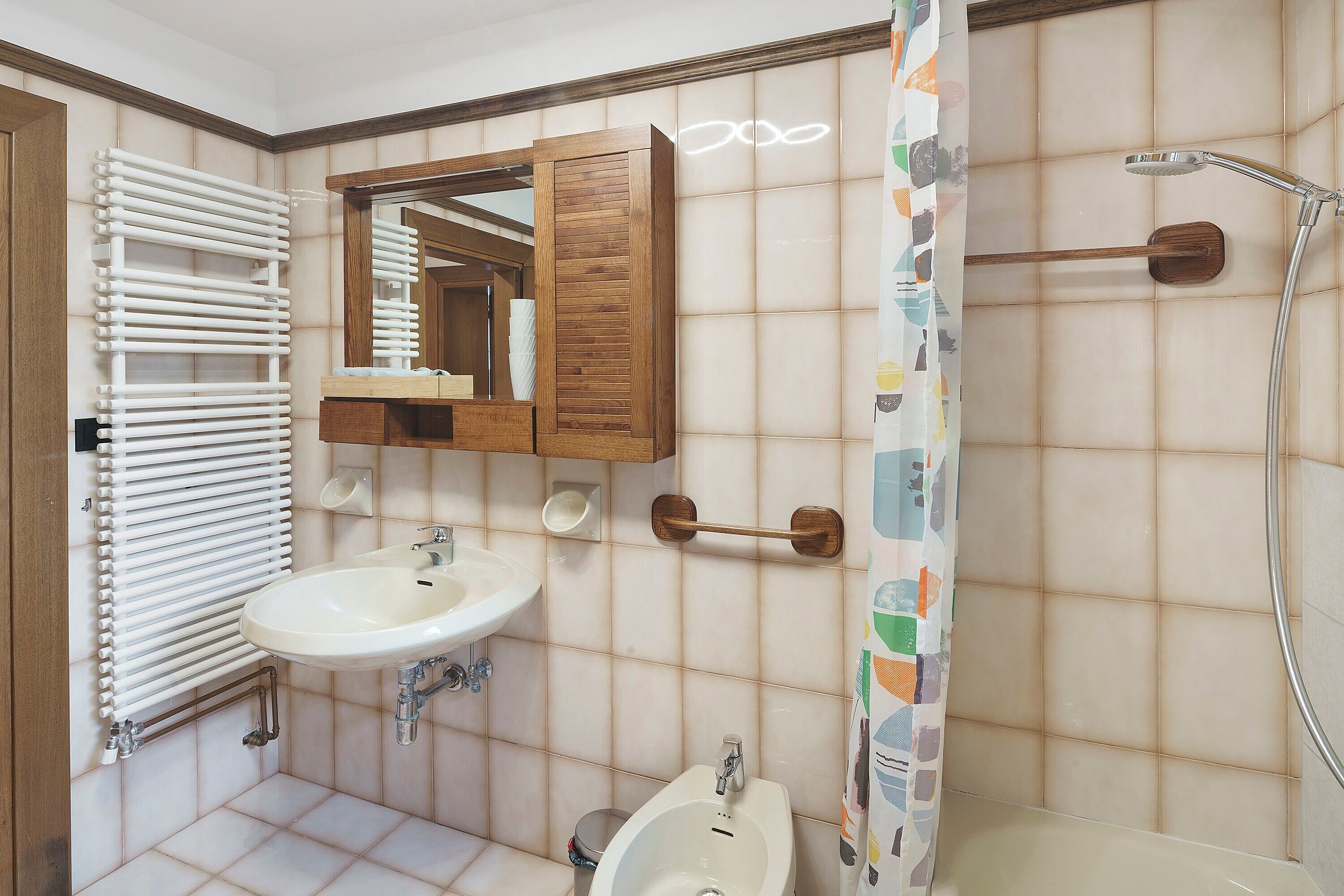 A bathroom with a white sink, a wooden cabinet, a mirror, a shower, and a toilet.