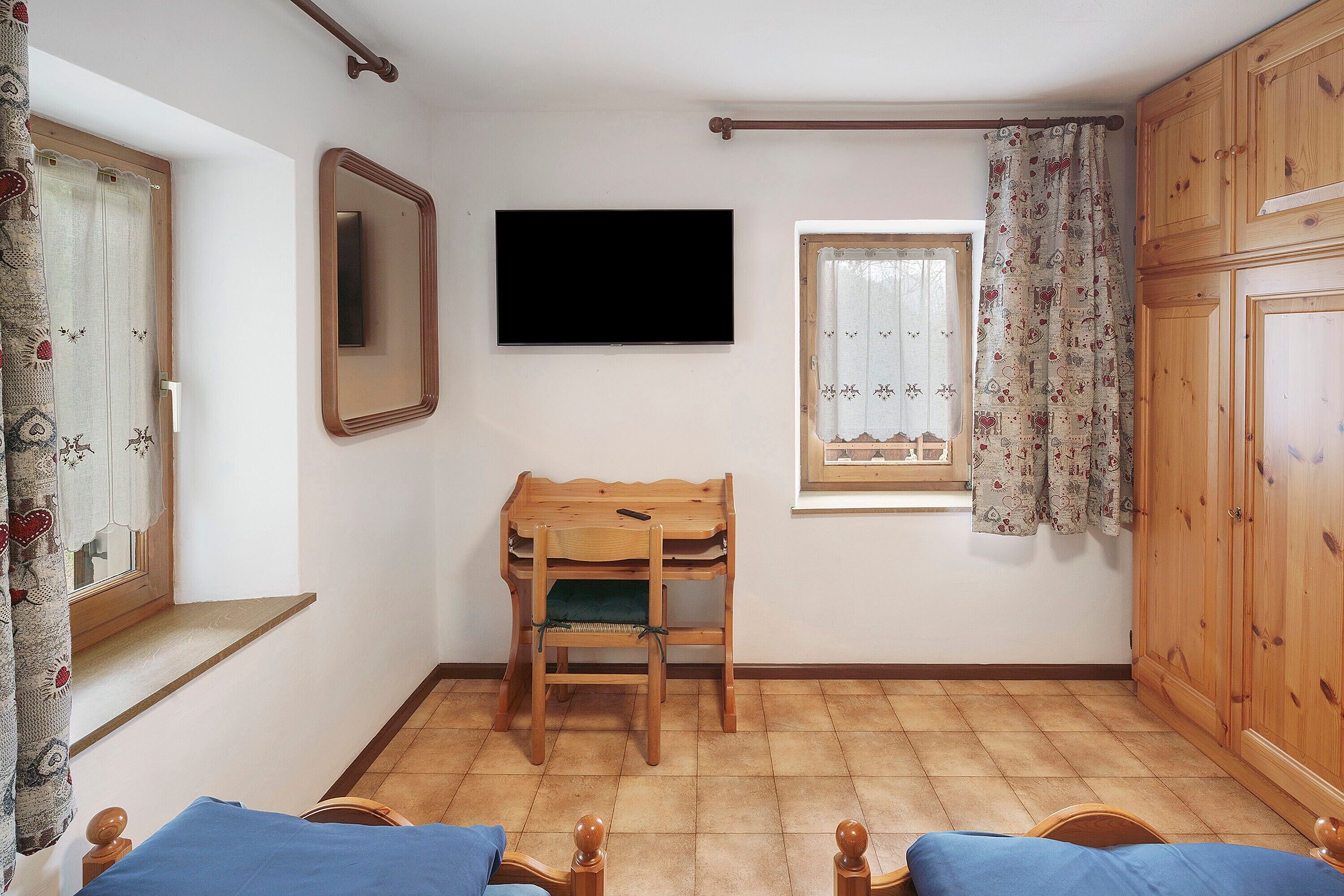 A room with a bed, a desk, a chair, a TV, a window, and a wardrobe.