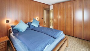 Een slaapkamer met een houten garderobe, een bed met blauw beddengoed en een nachtkastje.