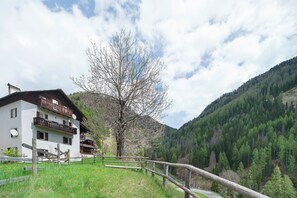 A two-story building with balconies, a wooden fence, and a mountain backdrop. - Apartment 'Sass De Stria' – Panoramic Views in the Dolomites near Arabba and Cortina (Cernadoi)