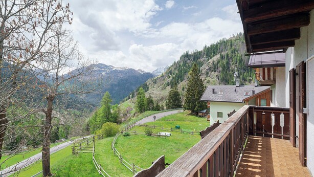 Een balkon met uitzicht op een berglandschap, een houten hek en een klein gebouw op de achtergrond.