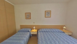 A room with two single beds, each with a bedside table and lamp. There are two framed pictures on the wall. - Prime Lignano Stay Close to the Sand (Lignano Sabbiadoro)