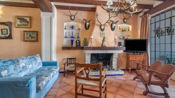 Una sala de estar con sofá, sillas, chimenea, monturas de animales y televisor.
