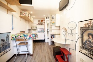 A compact kitchen with a dining area, wooden shelves, and a television. - Bright window - Vico Angeli 13 (Genova)