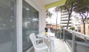A balcony with a table and chairs, a potted plant, and a view of buildings. - Your Ideal Beach Retreat With Terrace (Lignano Sabbiadoro)