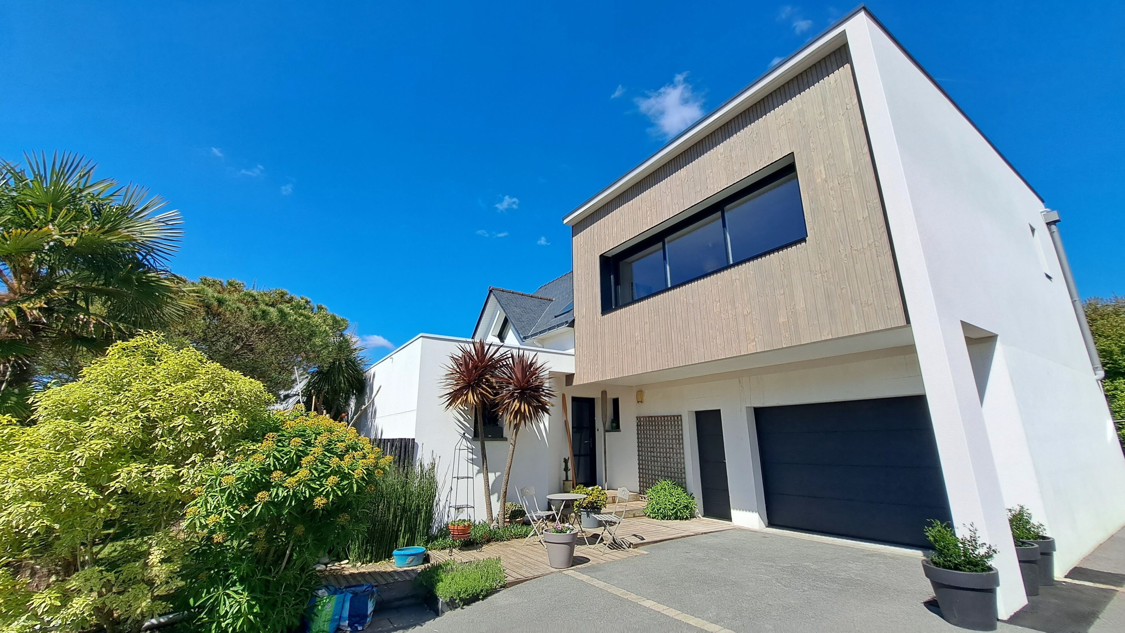 Ein modernes, zweistöckiges Haus mit Garage, umgeben von üppigem Grün und blauem Himmel.