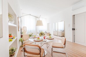 Ein heller, gut beleuchteter Essbereich mit einem runden Tisch, Korbstühlen und einer Hängeleuchte.