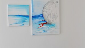 Un canapé de couleur turquoise agrémenté d’un coussin à motifs et de deux œuvres d’art représentant des scènes maritimes.