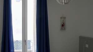 Une chambre à coucher comprenant un lit, des rideaux, un luminaire suspendu, une table de chevet et une lampe fixée au mur.
