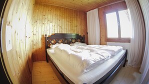 Een houten kamer met een bed, een raam met gordijnen en een houten plafond.