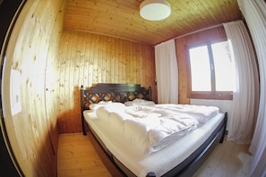 Une pièce en bois avec un lit, une fenêtre avec des rideaux et un plafond en bois.