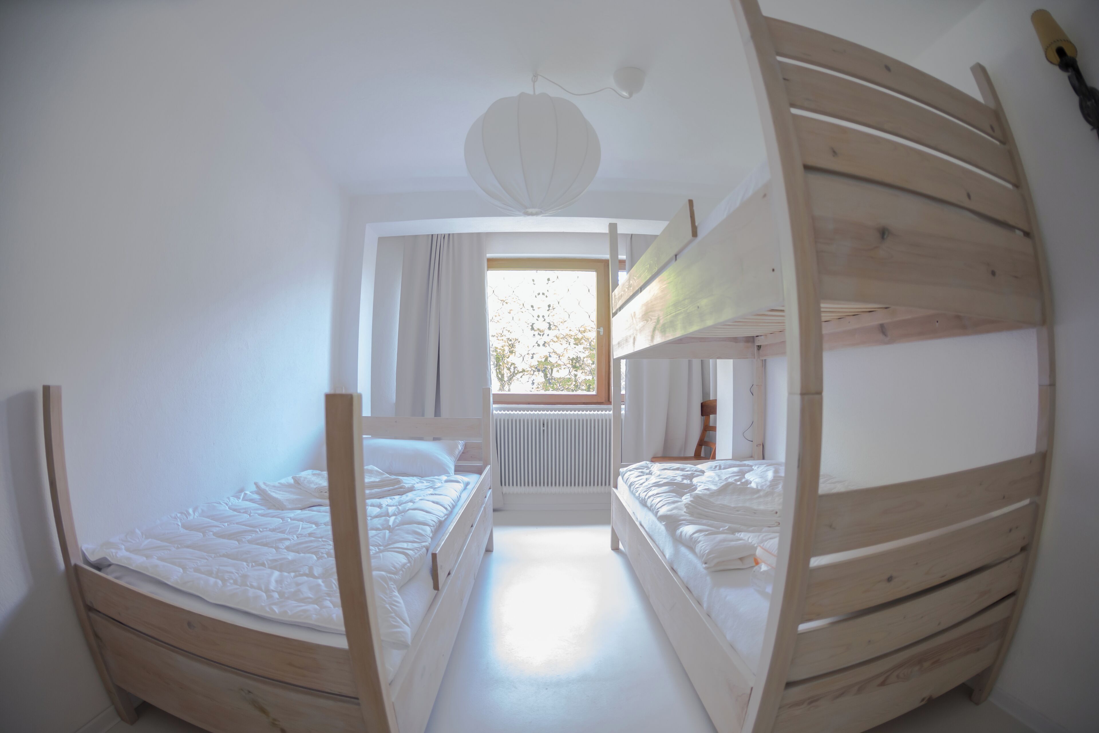 Ein Zimmer mit Etagenbetten, einem Heizkörper, einem fenster mit Vorhängen und einer Deckenleuchte.
