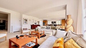 A spacious living area with a sofa, coffee table, and a dining table. There is a kitchen in the background with a view of the outdoors. - 6 bedroom villa completely renovated in 2026 located between sea and countryside ✨ (Ramatuelle)