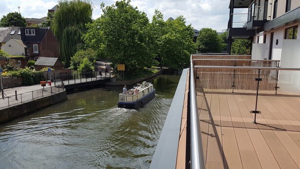 Un río con un bote, una cubierta de madera y edificios al fondo.