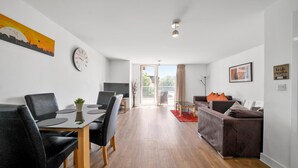 Una sala de estar moderna con comedor, piso de madera, un ventanal y un cuadro de paisaje urbano.
