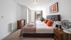 Un dormitorio moderno con una cama grande, una mesita de noche con lámpara, un ventilador y vistas al exterior.