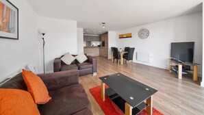 Una sala de estar moderna con un sofá marrón, un tapete rojo, una mesa de centro negra y un televisor sobre un mueble de madera.