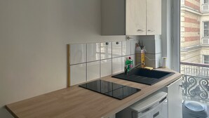 A kitchen with a wooden countertop, a black induction cooktop, a white cabinet, and a window with a view of buildings. - La Folie Urban Room R Publique Marais Canal St Martin (Paris)