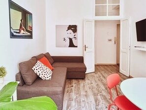 A living room with a brown sectional sofa, a dining table with red chairs, a TV mounted on the wall, and a door leading to another room. - DaliTourism - Colosseum Experience 28 (Roma)