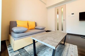 A modern living room with a sofa, a coffee table, a rug, and a TV mounted on the wall. - Crecia Doutonbori (Osaka)