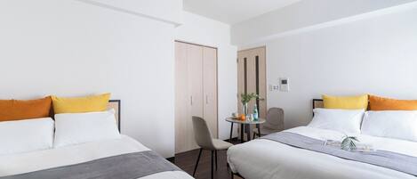 Une chambre d’hôtel avec deux lits, une petite table avec une chaise, une porte et un luminaire au plafond.