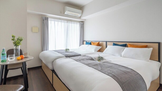 Ein Hotelzimmer mit zwei Betten, einem kleinen Tisch mit Vase und Obst, sowie einer Klimaanlage.