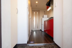 A narrow hallway with a red kitchen area, a white door at the end, and a marble floor. - Crecia Doutonbori (Osaka)