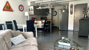 Ett modernt vardagsrum med en soffa, ett soffbord i glas och ett köksområde i bakgrunden.