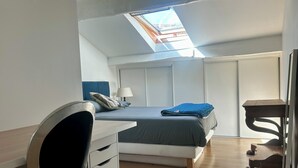 Ett rum med en säng, ett skrivbord, en stol, en lampa och ett takfönster.