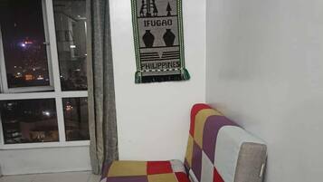 A room with a checkered sofa, a window with a view of city lights, and a wall-mounted poster.