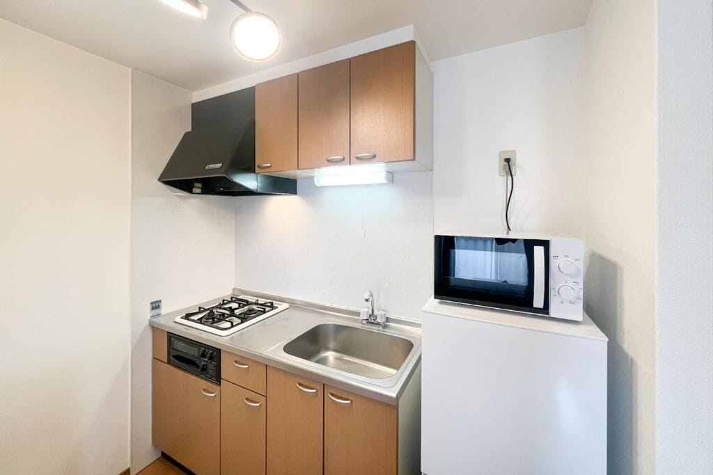 A compact kitchen with a gas stove, sink, microwave, and wooden cabinets.