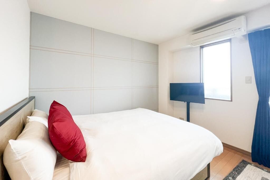 Habitación de hotel con cama, ventana con cortinas, aire acondicionado instalado en la pared y televisión de pantalla plana.