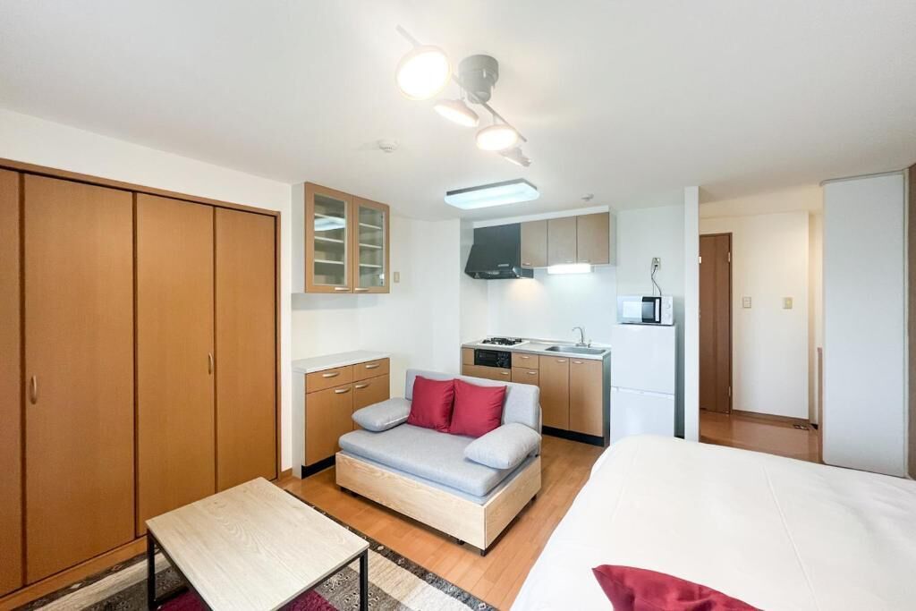 Et kompakt værelse med seng, sofa, lille bord, tekøkken og garderobeskab.