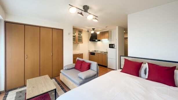 Een kleine hotelkamer met een bed, een slaapbank, een tafeltje, een kitchenette en een kledingkast.