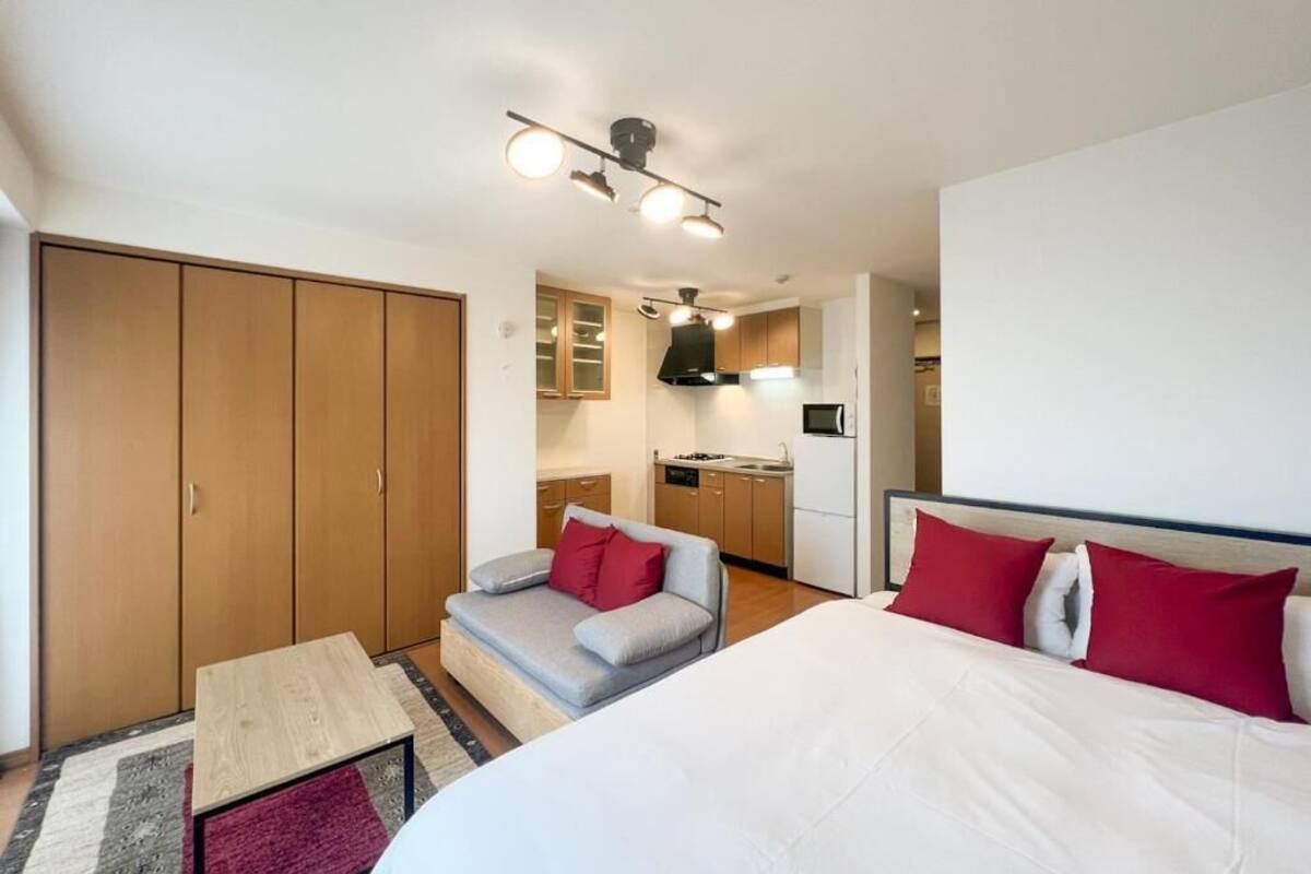 A compact hotel room with a bed, a sofa, a small table, a kitchenette, and a wardrobe.