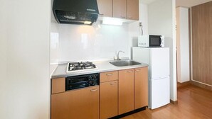 Een kleine keuken met een gasfornuis, spoelbak, magnetron en een witte koelkast.