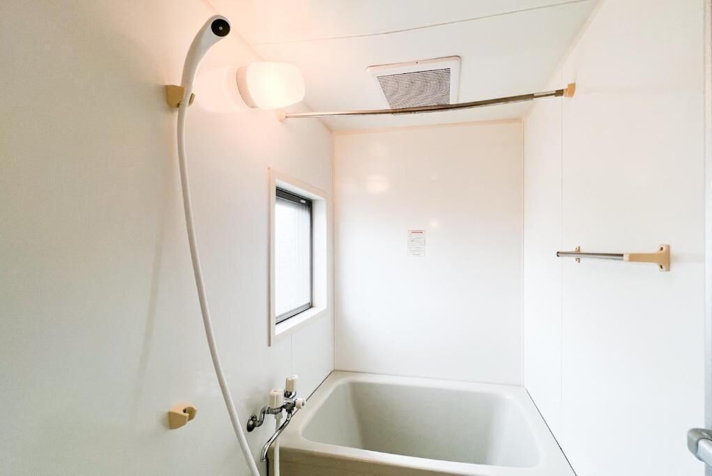Un baño pequeño y blanco con bañera, una ventana y un perchero para toallas.