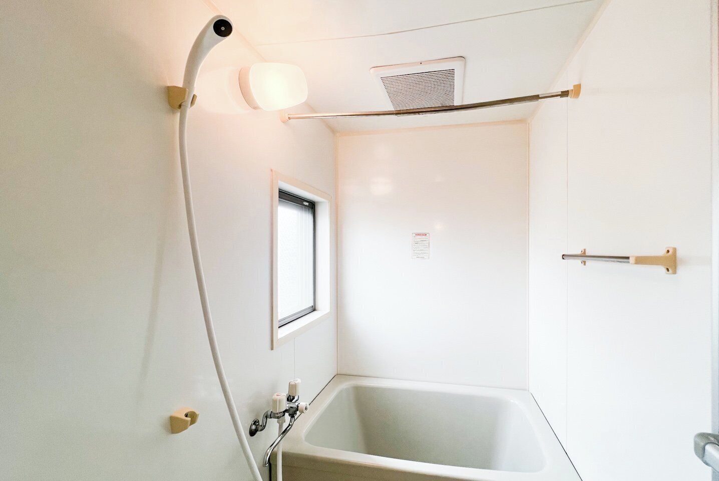 A bathroom with a bathtub, a showerhead, a window, and a towel rack.