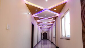 A hallway with a reflective tiled floor, recessed ceiling lighting, and a series of windows along one side. - Shubharambh Green's (Vrindavan)