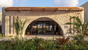 Un edificio de piedra con un porche de pérgola de madera, rodeado de plantas tropicales.