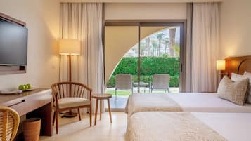 Habitación de hotel con cama, escritorio con televisor, silla, mesa pequeña y vista a un jardín por una puerta corredera.