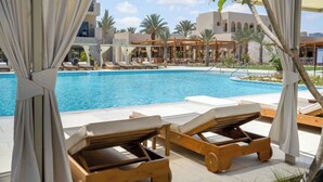 Zona de piscina con sillones reclinables y vista a un edificio con varios balcones.