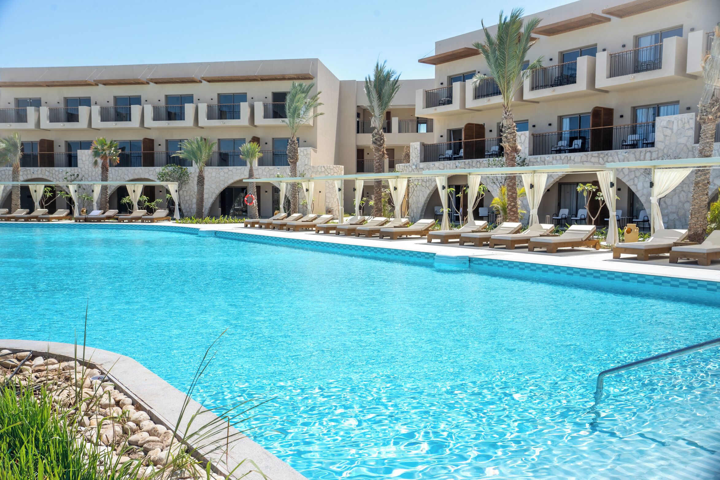 A hotel pool area with multiple lounge chairs and a clear blue pool.