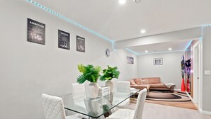 En moderne stue med et glasbord, hvide stole, en sofa og dekorative planter.