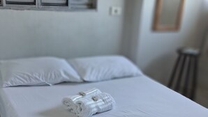 A neatly made bed with white linens and a rolled towel, a window with blinds, and a small stool. - Pousada Serra Azul (Juquiá)
