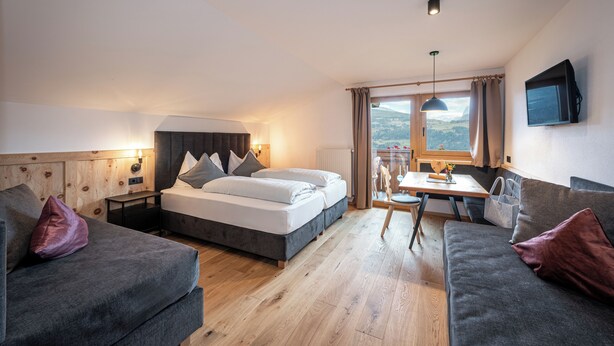 Ein modernes Hotelzimmer mit einem Bett, zwei Sofas, einem Esstisch und einem Fernseher.