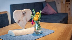 Ein herzförmiges Holzobjekt auf einem Tisch mit einer klaren Glasvase, die gelbe Blumen enthält.