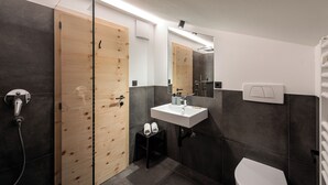 Ein modernes Badezimmer mit Holztür, Waschbecken in Weiß, Spiegel und Dusche.